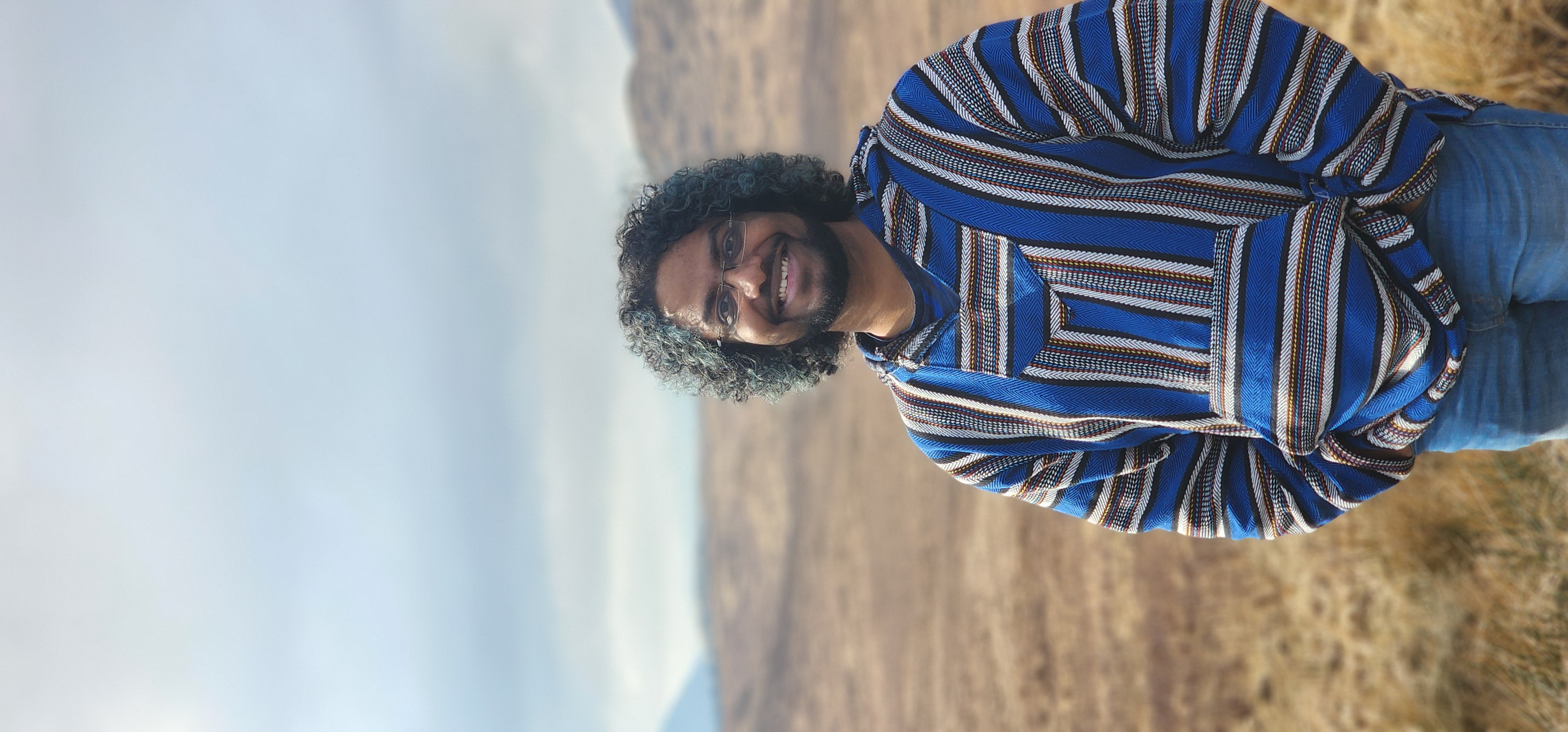 Arjun Madhusudan smiling outdoors in a mountainous landscape.