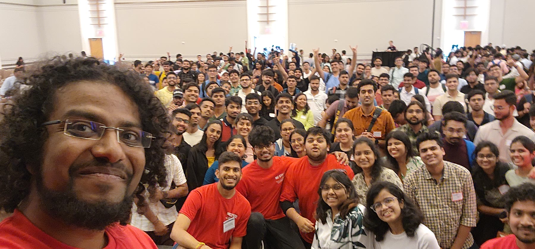 Arjun taking a group selfie with Maitri IGSA members and attendees at a crowded NC State event