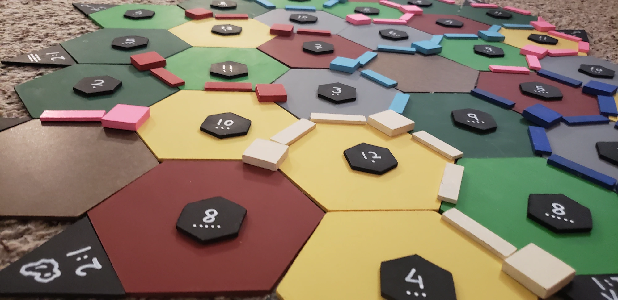 A handmade Catan board with painted wooden terrain, roads, buildings, and numbered tokens.