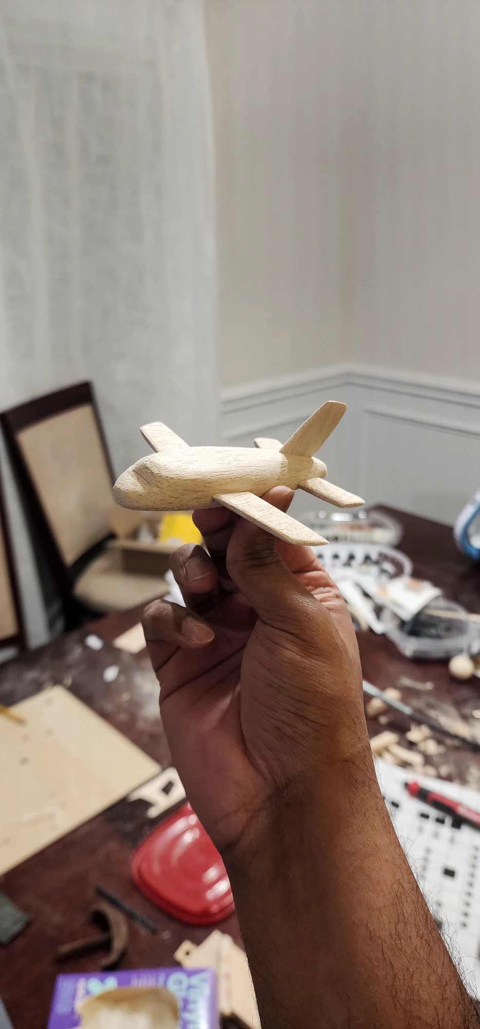 A small hand-carved wooden airplane held above a table scattered with tools and materials.
