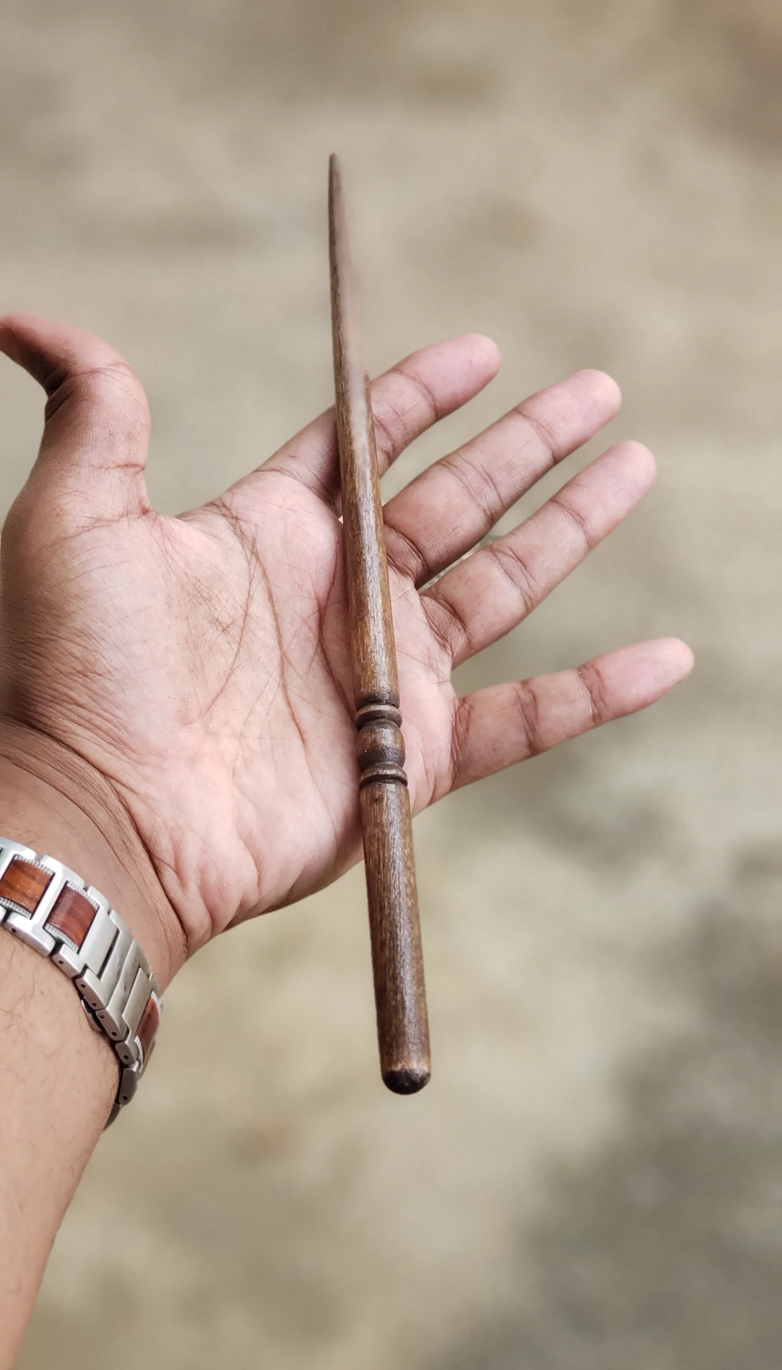 A hand holding a finished slender wooden wand with a carved handle.